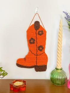 an orange crocheted boot hanging on a wall next to a candle and vase