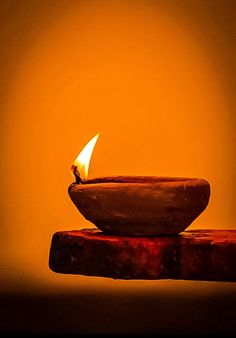 a small lit candle sitting on top of a wooden stand in front of a yellow wall