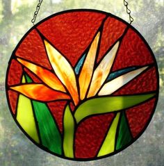 a stained glass flower hanging from a chain on a window sill in front of a tree