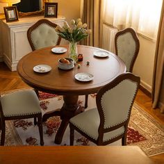 a dining room table with four chairs and plates on it, in front of a window