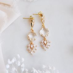 two pairs of gold tone earrings with clear crystal stones on top of white flower petals