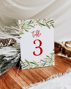 a table number sitting on top of a wooden table next to pine cones and candles