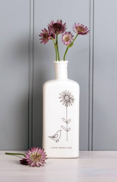 a white vase with flowers in it sitting on a table next to a purple flower