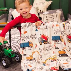 a young boy holding onto a blanket with construction trucks on it