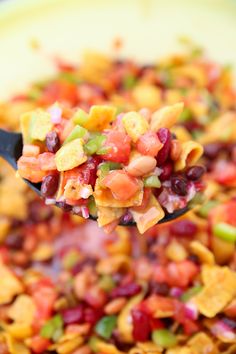 a spoon full of fruit salad on top of a yellow bowl filled with cereal and veggies