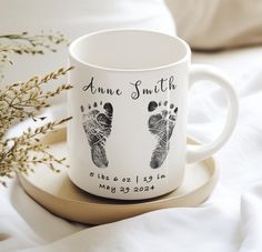 a personalized coffee mug sits on a tray next to a flower vase and some baby's footprints