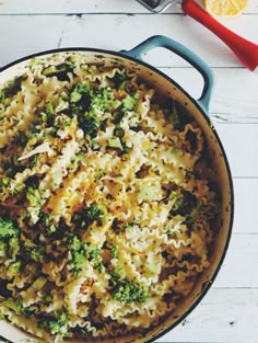 a pot filled with pasta and broccoli on top of a white wooden table