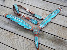 a blue and white horse bridle with feathers on it's side, sitting on a wooden deck