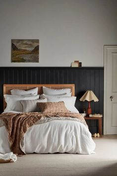 a bed with white sheets and pillows in a bedroom next to a painting on the wall