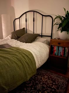 a bed with green blankets and pillows in a bedroom next to a book shelf filled with books