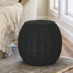 a large black basket sitting on top of a rug next to a white chair and pillows