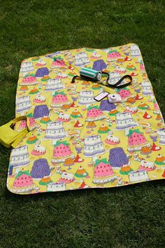 a yellow picnic blanket with scissors and other items on it sitting in the green grass