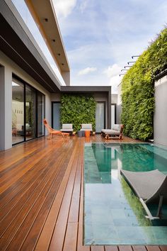 a wooden deck next to a swimming pool with lounge chairs and plants growing on the wall