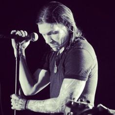 a man with long hair and tattoos on his arm holding a microphone in front of him