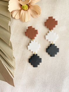 the pixel earrings in black, white and brown are on display next to a flower