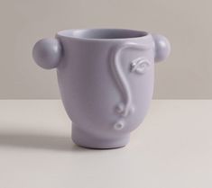 a white cup sitting on top of a table next to a vase with a handle