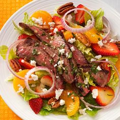 a white plate topped with meat and salad next to sliced oranges, strawberries and pecans