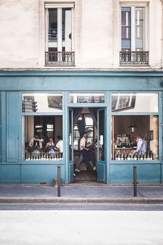 people sitting at tables in front of a blue building with glass doors and windows on both sides