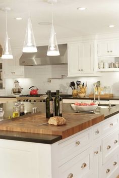 a kitchen with white cabinets and wooden counter tops, an island in the middle has wine bottles on it