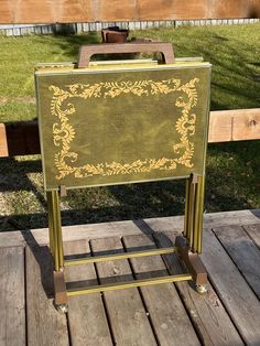 a green and gold easel sitting on top of a wooden deck next to a field