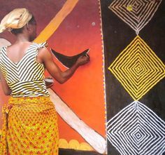 a woman is standing in front of a wall with different colored designs on it and holding a piece of wood