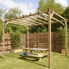 a wooden pergolan in the middle of a yard with picnic table and benches