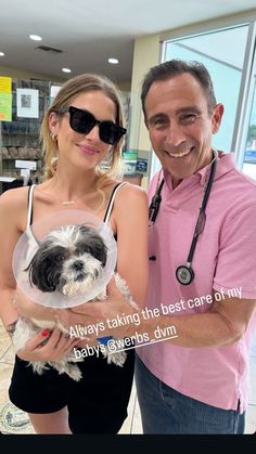 a man standing next to a woman holding a small dog wearing a cone on her head