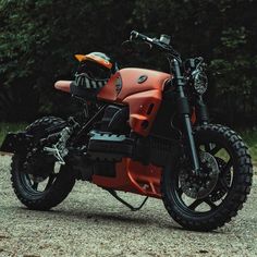 an orange and black motorcycle parked on top of a gravel road next to some trees