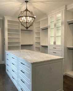 an empty walk in closet with white cabinets and marble counter top, chandelier hanging from the ceiling