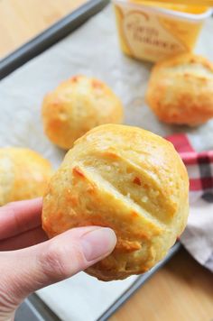 a person holding a muffin in front of some other muffins on a baking sheet