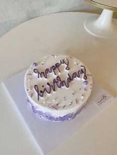 a white cake with purple sprinkles on it that says happy birthday sitting on a table