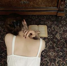 a woman laying on the floor reading a book with her head resting on an open book