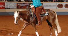 a woman riding on the back of a brown and white horse in a dirt arena