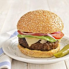 a hamburger with lettuce, tomato and cheese on a plate next to a pickle