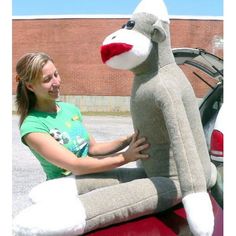 a woman sitting on the back of a red car next to a stuffed animal monkey