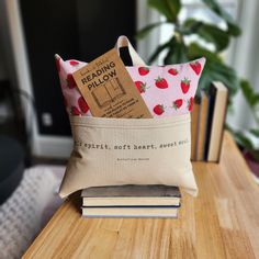 a small pillow sitting on top of a wooden table next to books and a plant