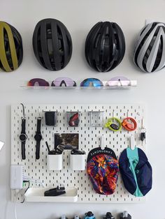 several different types of helmets hanging on a white wall with pegs and wires attached to it