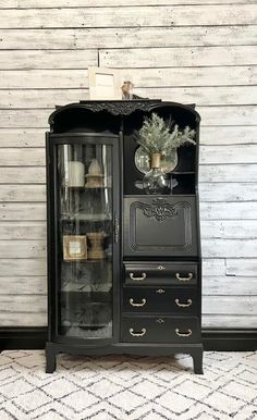 an old fashioned black china cabinet with glass doors and drawers in front of a white wall