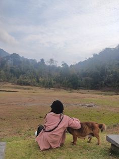 a person sitting on the ground with a dog in front of them looking at something