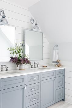 a bathroom with two sinks, mirrors and flowers in vases on the counter top