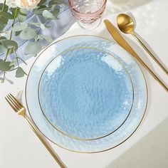 a blue plate with gold rim sits on a white tablecloth next to silverware and flowers