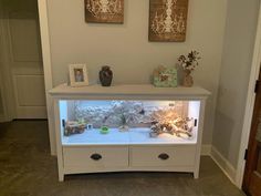 a white cabinet with two pictures on top and an aquarium in the bottom, along with other items