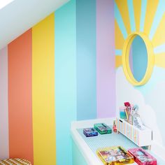 a room with colorful stripes painted on the wall and a mirror above it, along with toys