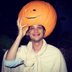 a man wearing a pumpkin hat on top of his head while holding it up to his face