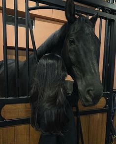 a woman standing next to a black horse in a stall with its head over the gate