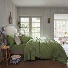 a bed with green sheets and pillows in a white room next to a wooden floor