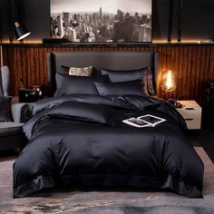 a bed with black comforter and pillows in a room next to a gray chair