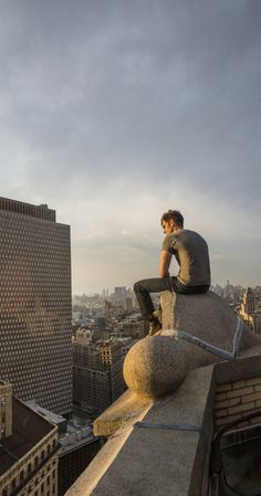 a man sitting on top of a building next to a tall building in the city