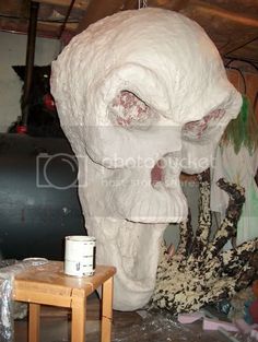 a large white skull statue sitting next to a wooden table with paint on it's face