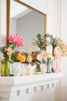 a mantle with vases and flowers on it, along with a mirror above the mantel